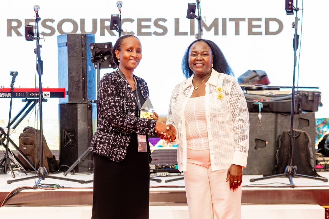 Fiona Ntoreine shakes hands with a presenter on stage while holding a crystal pyramid trophy.